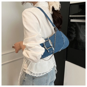 Detail of blue denim shoulder bag featuring silver buckle, fringe edges and metal chain