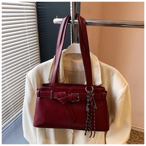 Detail view of burgundy leather shoulder bag with buckle and woven tassel on white blazer