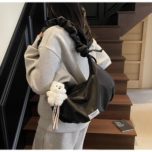 Detail of black nylon dumpling bag with scrunchie strap and white plush bear charm on a model