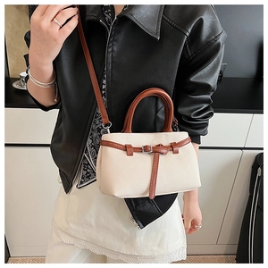 Detailed view of cream canvas bucket bag with brown leather trim and thin shoulder strap