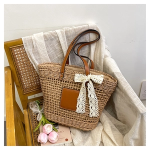 Detail of light brown straw tote bag with brown leather straps and white lace bow