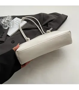 Detail of white leather shoulder bag featuring unique knotted handle and silver metal accents