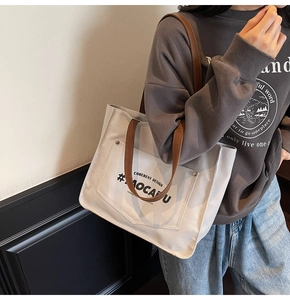 Detail of a minimalist canvas tote bag with brown straps and printed front pocket