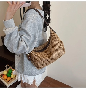 Détail du sac hobo en paille tressée avec bandoulière en cuir et pendentif perlé élégant
