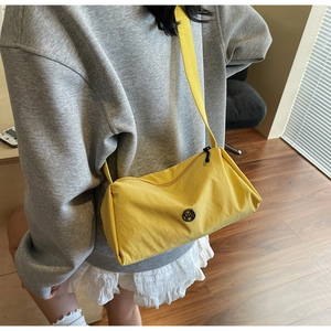 Detail of yellow nylon pillow bag featuring a circular metal M logo and matching strap