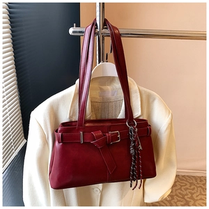 Detail of dark red vintage leather tote with metal buckle and decorative tassel charm