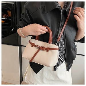 Detail of cream woven bucket bag with brown leather handles and decorative straps