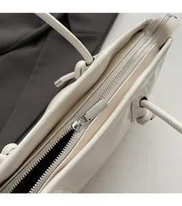 Close-up of a smooth silver metal zipper on a cream white glossy leather tote bag