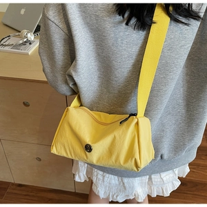 Detail of a bright yellow nylon crossbody bag featuring a round logo and wide strap