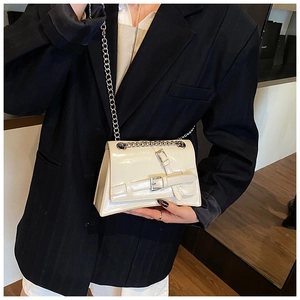 Detail of beige glossy crossbody bag with silver chain strap worn with a black blazer