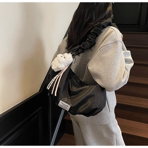 Detail of black pleated crescent bag with fashion label and plush bear keychain