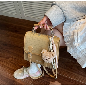 Détail du sac à dos beige imprimé avec plaque métallique et pendentif ours en peluche