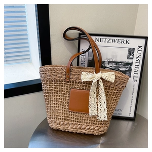 Detail of woven straw tote bag with brown faux leather handles and white lace bow