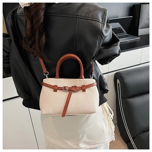 Detail of cream crossbody bucket bag with brown leather strap worn by a model in a modern office