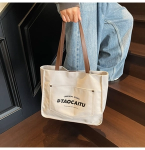 Detail of a large beige canvas tote bag with brown leather handles on wooden stairs