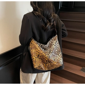 Detail of a large leopard print hobo bag worn by a model on dark wooden stairs