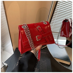 Detail of bright red patent leather handbag with silver buckle straps and chain strap