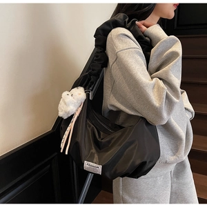 Side view of black nylon shoulder bag with ruffled strap and a plush bear charm