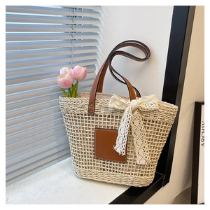 Close-up of woven straw tote bag with brown leather handles and delicate lace bow detail