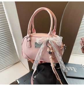 Detail der hellrosa Boston-Tasche mit weißer Spitzenschleife und Metallanhänger