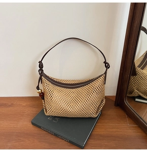 Détail du sac en paille tressée en demi-lune avec bandoulière en cuir et charmes décoratifs