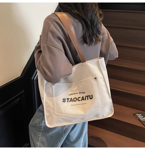 Detail of canvas tote bag with brown leather strap and elegant printed text on wood stairs