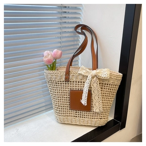 Detailed close-up of woven straw beach tote featuring lace bow and leather patch detail