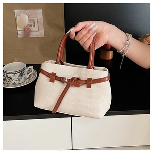 Close-up of cream canvas bucket bag featuring brown leather handles and belt buckle detail