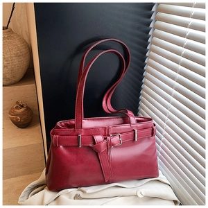 Artistic detail of burgundy faux leather shoulder bag with buckle strap on a textured step