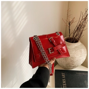 Close-up of bright red leather crossbody bag with silver chains and buckle details