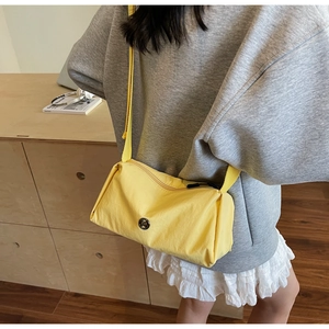 Detail of bright yellow nylon crossbody bag featuring a silver metal M logo and strap