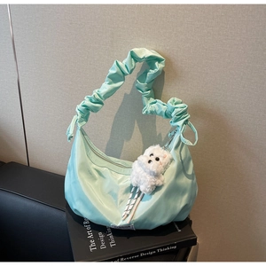 Detail of mint green nylon pleated bag with plush dog charm on design books