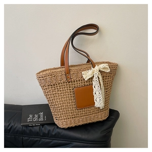 Detail of woven straw tote bag with brown leather patch and delicate white lace bow