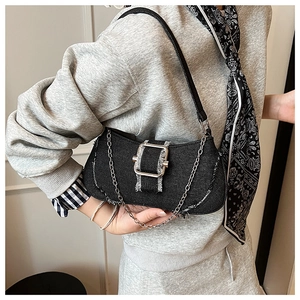 Detail of black denim bag featuring silver square buckle, raw edges and metal chain strap