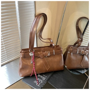 Close-up of retro brown tote bag with metal buckle and woven charm in soft natural light