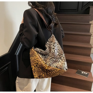 Detail of a large leopard print tote bag with brown leather straps held by a model
