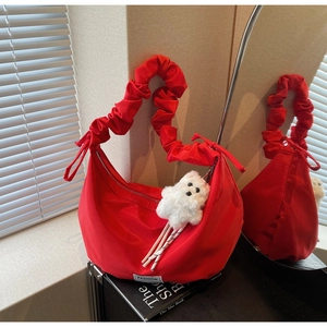 Detail of red nylon crescent bag featuring a ruched shoulder strap and white bear charm