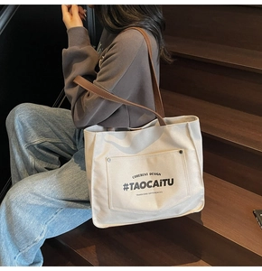 Close-up of a large canvas tote bag with brown leather straps on a wooden staircase