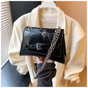 Detail of a black angular crossbody bag with silver chain and glossy faux leather texture