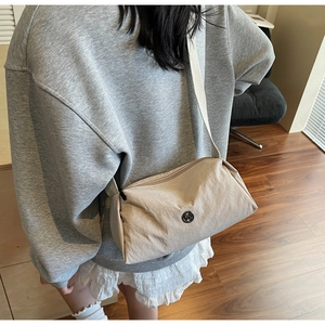 Close-up of beige crossbody bag showing pleated texture and round metal M logo badge