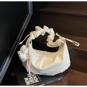 Detail of cream croissant bag featuring a scrunchie handle and plush charm on wood steps