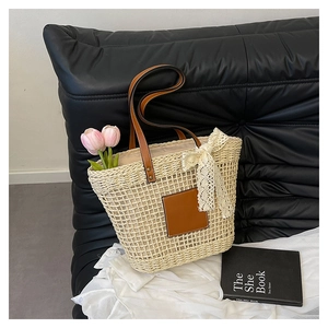 Detail of woven straw tote bag with brown leather handles and delicate lace bow