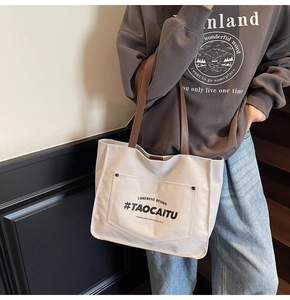 Detail view of large canvas tote bag with brown leather straps and front pocket