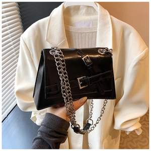 Detail of glossy black leather crossbody bag with bold silver chain and buckle strap