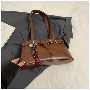 Detail of caramel brown leather shoulder bag with buckle, bow, and woven charm detail