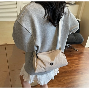 Detail of a beige pleated nylon crossbody bag with metal logo on a model in a cozy room