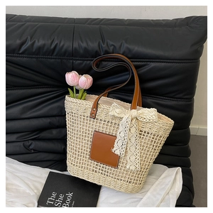 Close-up of beige woven straw tote bag with brown leather handles and a lace bow detail