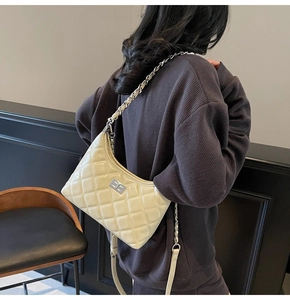 Rückansicht der cremefarbenen Stepptasche mit Silberkette auf grauem Sweatshirt