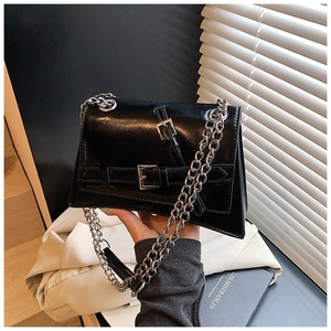 Detail of glossy black shoulder bag featuring dual silver chains and buckle straps