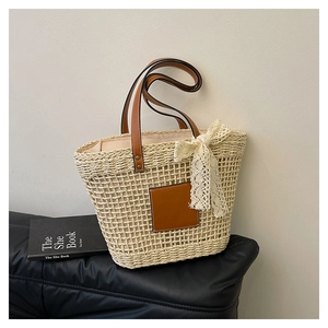 Detail of woven straw tote bag with brown leather patch and white lace bow decoration